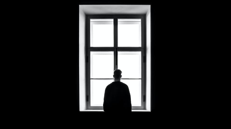 Mann steht alleine vor Fenster.
