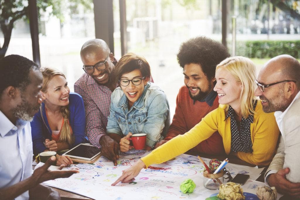Auf dem Bild ist eine Gruppe von Menschen zu sehen, welche gemeinsam am Tisch sitzen und auf einem White Board ein Brainstorming durchführen.